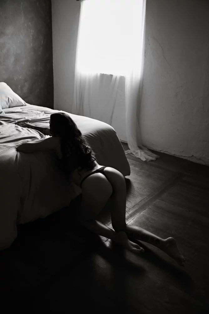 Image of image of a woman kneeing in front of a bed for a boudoir photo shoot