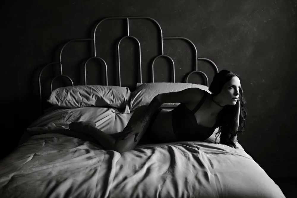 Image of black and white photo of a woman laying on a bed in lingerie